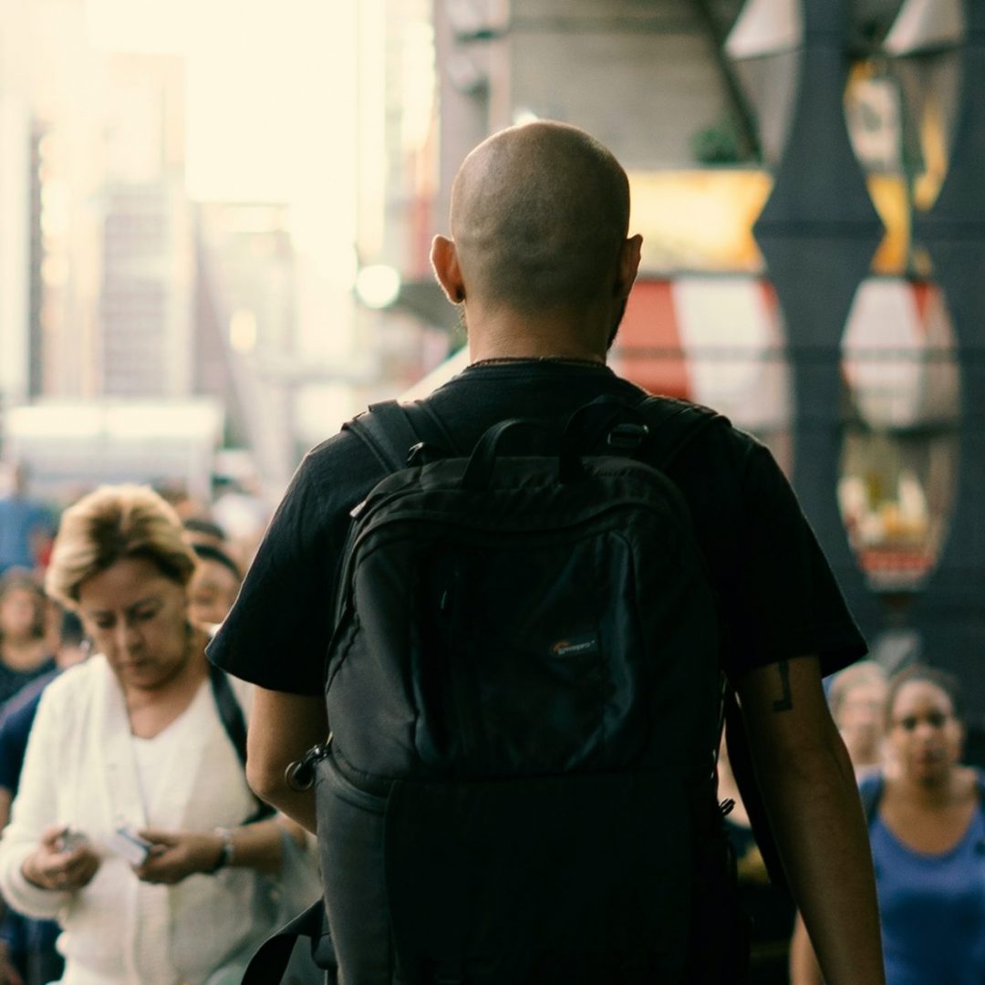 Rapaz de mochila andando em meio a multidão - Instituto Locomotiva de Pesquisa